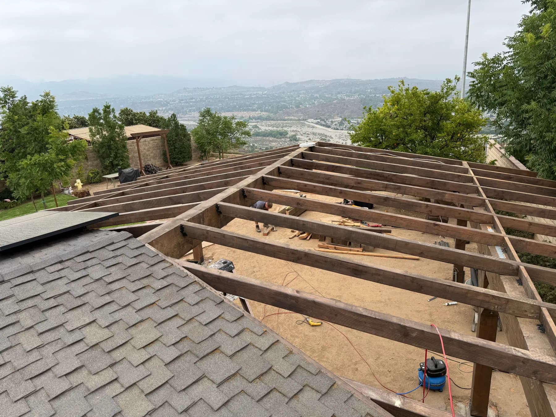 Roof framing in progress on a hillside build with the Santa Clarita Valley in the distance.