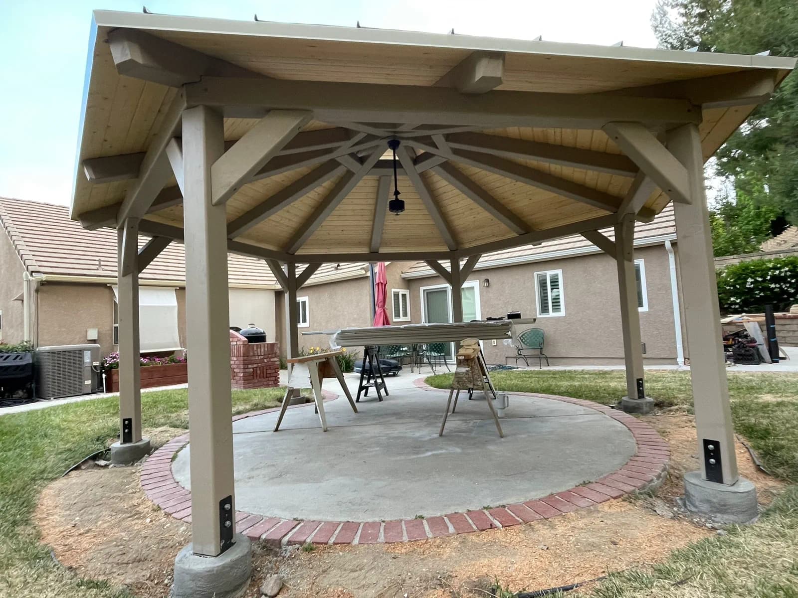 Finished cedar gazebo with a star pattern wood ceiling over a circular concrete pad with brick edging.