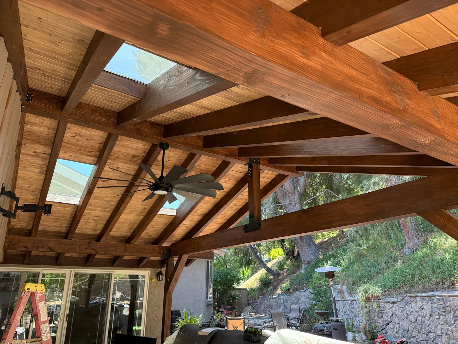 Underside of a finished patio cover with a stained tongue and groove ceiling, exposed beams, and skylights.